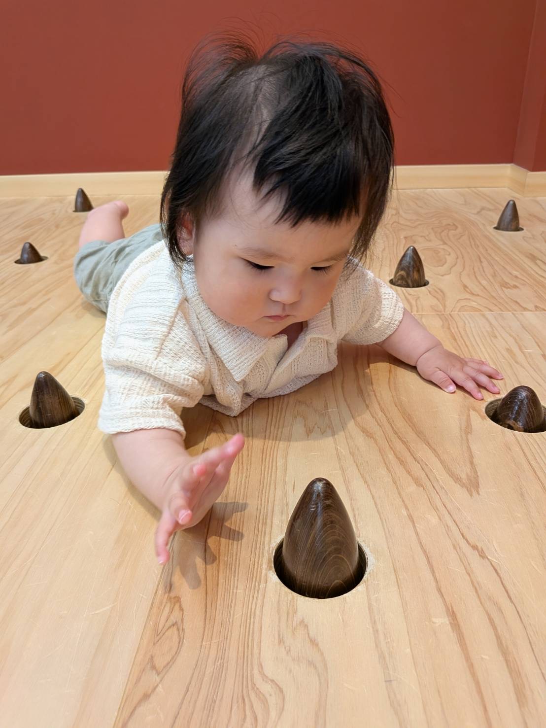 木の床でハイハイしながら木のおもちゃへ手を伸ばす赤ちゃん